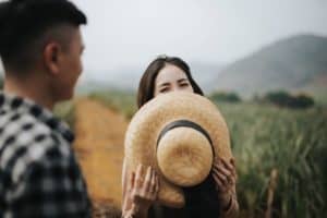 woman hides her smile behind a hat